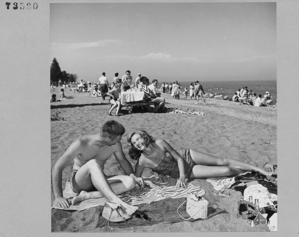 A black-and-white photograph of Kathleen Hart and Dave Phipps sunbathing on the beach. 