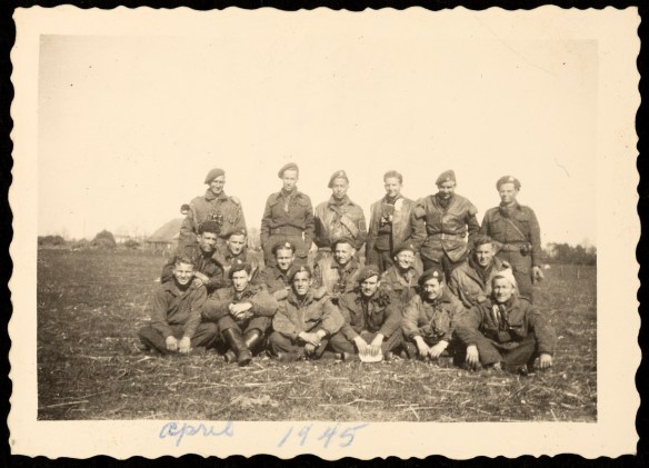 A black-and-white photograph of a group of 18 soldiers in uniform in a tilled field.