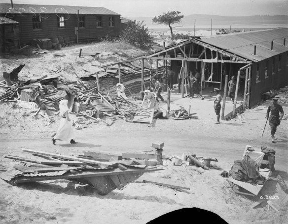 A black-and-white photograph of nursing sisters and uniformed soldiers cleaning up the debris from a hospital ward that has been damaged.