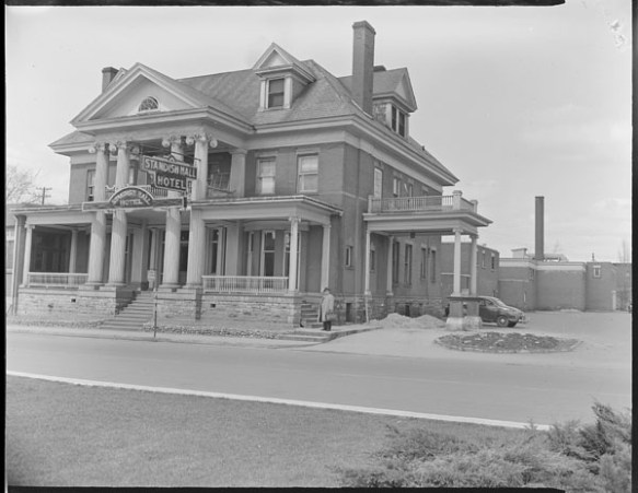 A black-and-white photograph of a large building, with a wide veranda and a sign reading “Standish Hall Hotel.”