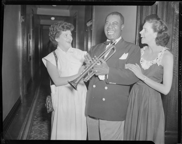 A black-and-white photograph of two women with a man holding a trumpet. 