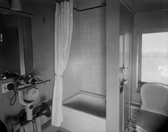 A black-and-white photograph of a shower, bath and toilet in a train lounge car.