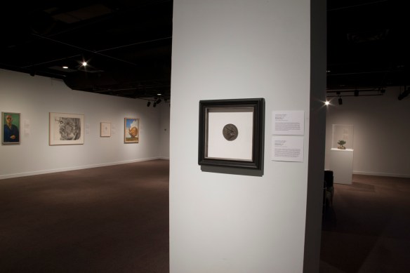 A colour photograph of a dimly lit room with various art pieces hung on the walls.