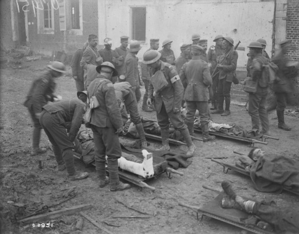 A black-and-white photograph of stretcher-bearers and medical personnel caring for wounded soldiers while other soldiers are standing around in the background.