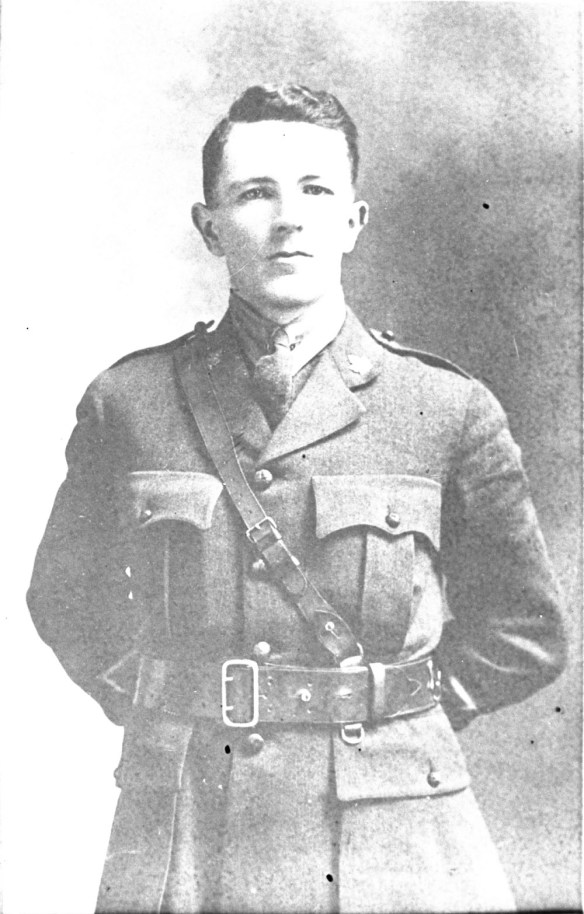 A black-and-white photograph of an officer wearing a Sam Brown belt, with his hands behind is back.