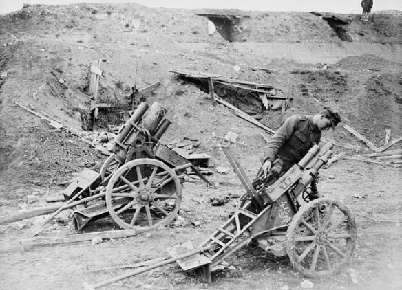A black-and-white photograph of large mortars pointing upward, as a soldier leans over one to look down its barrel.