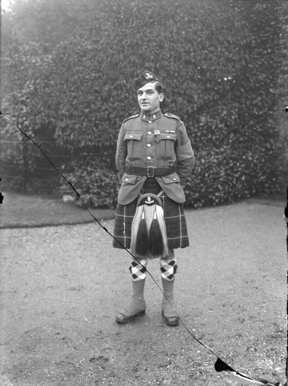 A black-and-white photograph of a standing soldier wearing a kilt. 