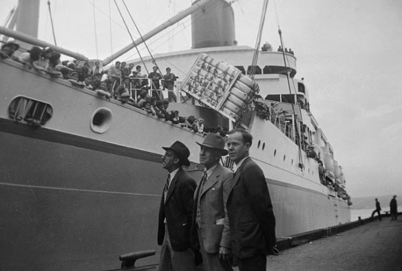 A black-and-white photograph of three men standing in front of a ship.