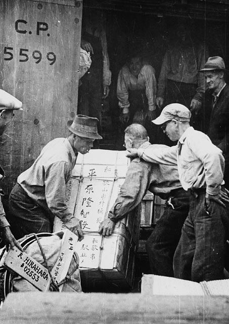 A black-and-white photograph of three men lifting a crate.
