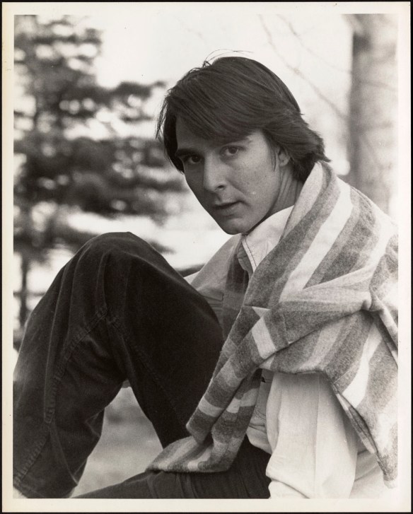 Black-and-white photo of a young man sitting with a sweater across his shoulders. 