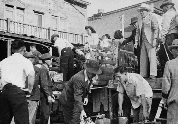 A black-and-white photograph showing twelve Japanese Canadians unloading a truck.