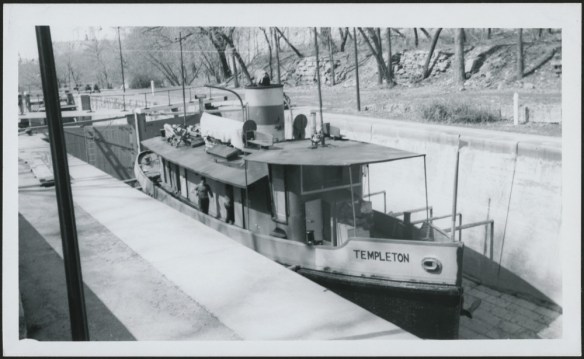 A black-and-white photograph of a medium-sized boat in the process of crossing a system of locks. 