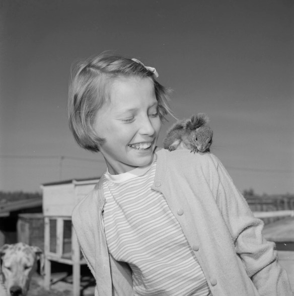 A black-and-white photograph of a girl and a squirrel on her left shoulder. 