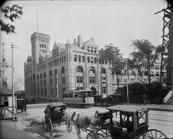 A black-and-white photograph of a trolley car, and horses and carriages outside Windsor Station, Montréal, Quebec. 