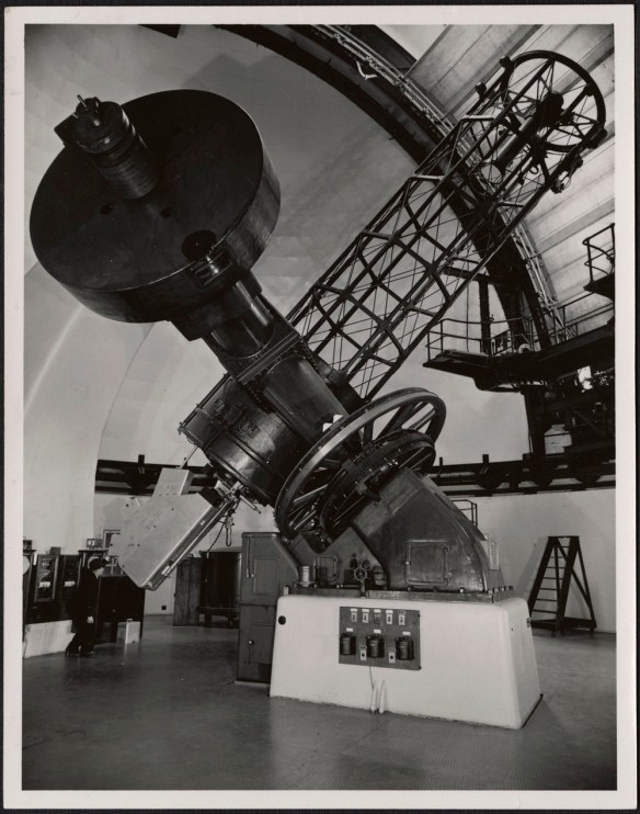A black-and-white photograph of a man looking into the eyepiece of Victoria’s Dominion Astrophysical Observatory Telescope. 