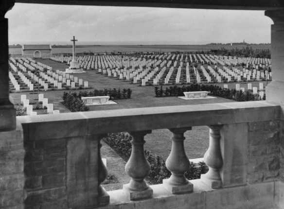 A black-and-white photograph showing many rows of Imperial War Graves Commission headstones, and a large Cross of Sacrifice.