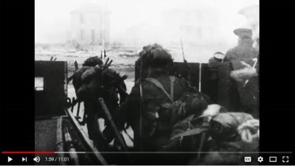 A black-and-white image taken from moving film, showing soldiers exiting a landing craft.