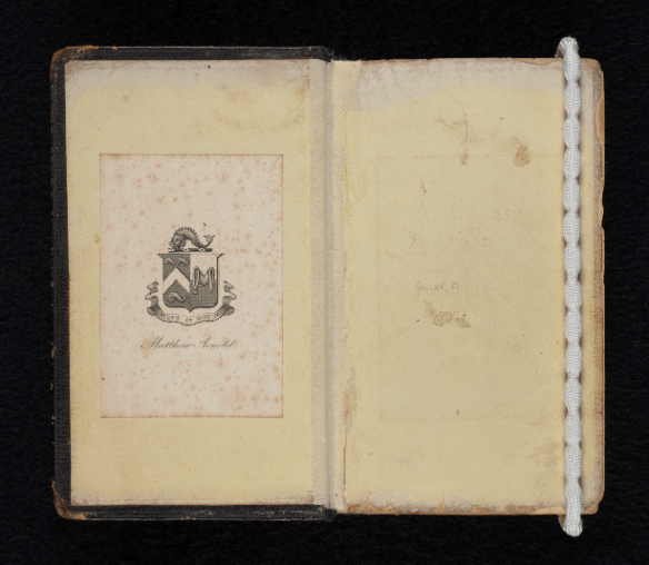 A book open to the inside front cover. Attached to the left-hand page is the bookplate of Matthew Arnold. The right-hand page is blank and held down by a weight.