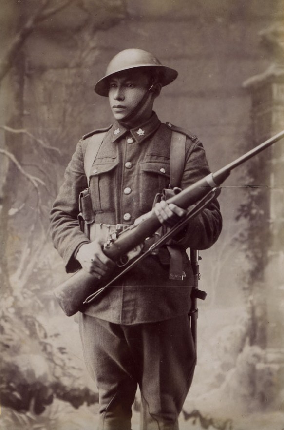 A black-and-white studio portrait of a First World War soldier in uniform and holding a rifle. 