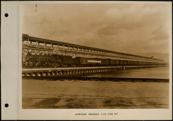 Photograph of a train at a pier, with a banner on a sign indicating that the train has a special shipment of Japanese oranges.