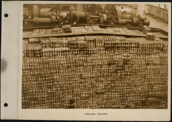 Photograph of workers with hundreds of crates of oranges on a ship deck.