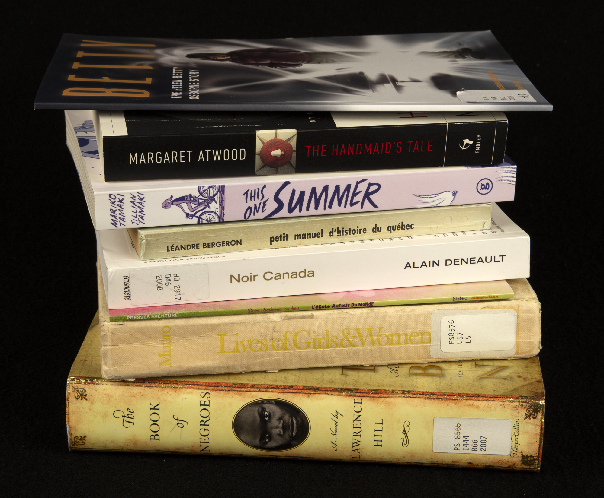 A colour photograph showing the spines of a stack of books against a black background.