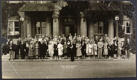 Large group of men and women standing in front of the entrance to a building.