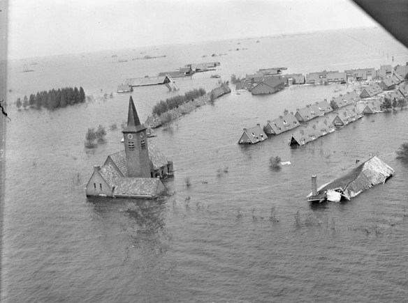 Flooded village with rooftops and a church steeple protruding from the waters.