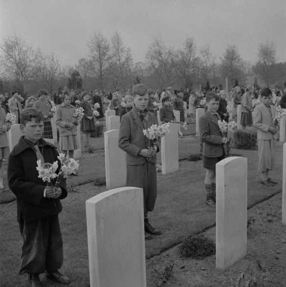Several children standing in front of headstones, holding bouquets of daffodils.