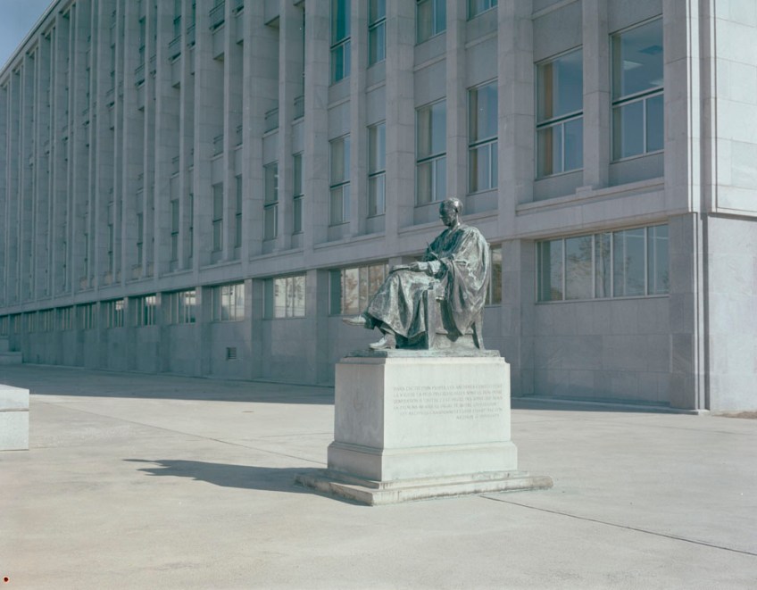 Colour photo of a statue of a seated man with a large building in the background.