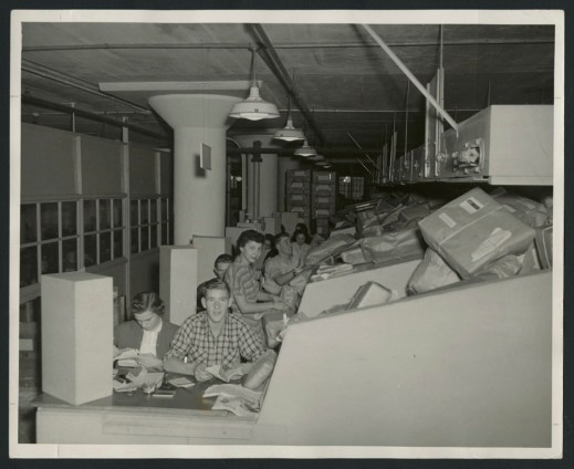 Two black-and-white photographs, one showing a group of employees sorting parcels into bins, and the other showing women at desks checking addresses on parcels as the parcels slide down a ramp toward them.