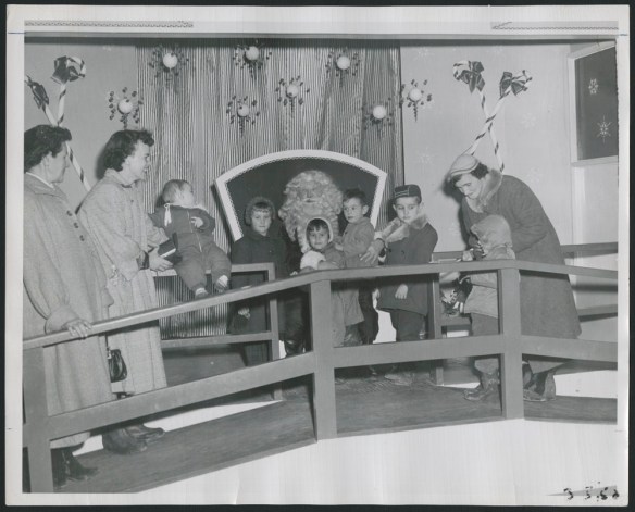 Black-and-white photograph showing children lined up to see Santa Claus, together with three adult women. Everyone is smiling, although some of the children look nervous.
