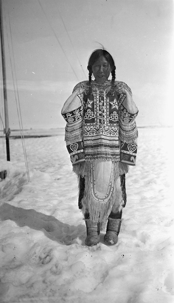 A black-and-white photo of an Inuk woman wearing a decorated parka standing in snow.