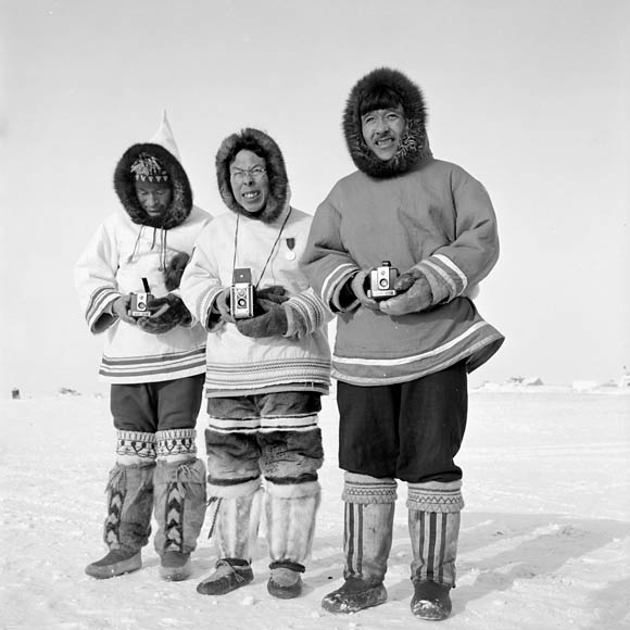 Black-and-white photo of three Inuit men standing outside in the winter. All three are dressed in traditional clothing.