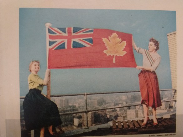 A colour photograph of two women holding a flag on a rooftop.