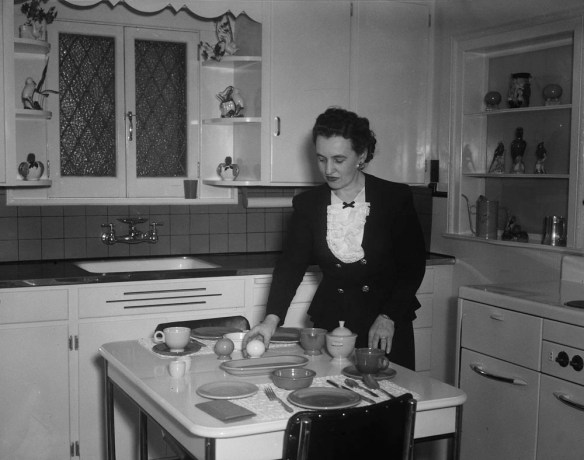 Black-and-white photo of a woman setting the kitchen table.