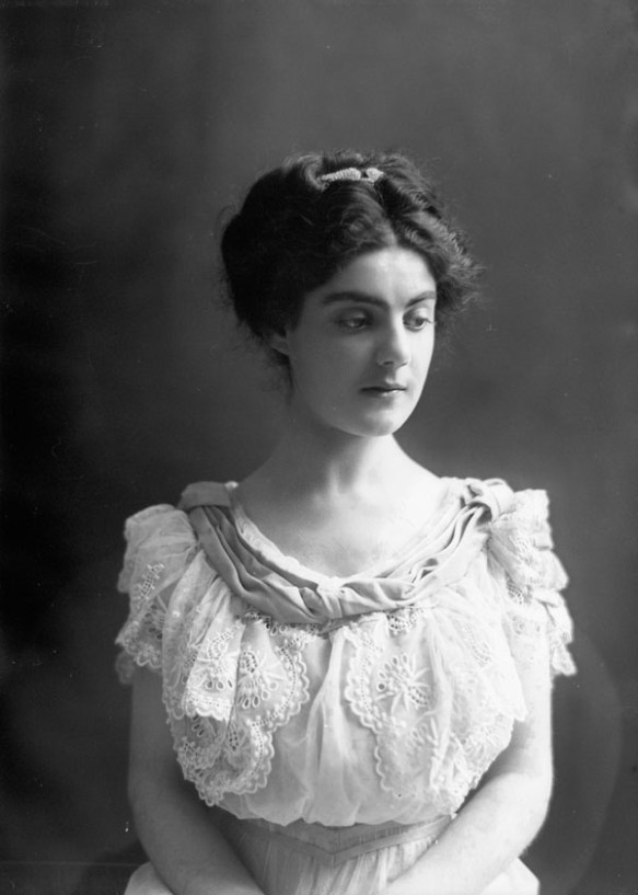 Black-and-white photo of a young woman in a white lace dress, facing the camera. 