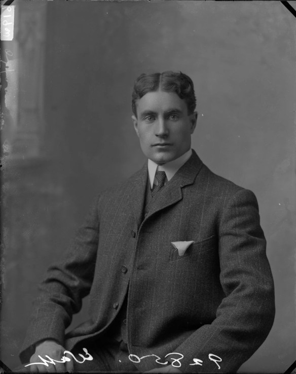 Black-and-white photo of a man in a dark suit, facing the camera. 