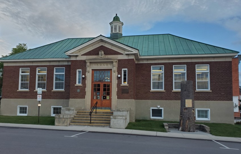A colour photo of a one-storey building with brown-brick exterior walls and a green roof. A small set of stairs and a railing lead up to the entrance.