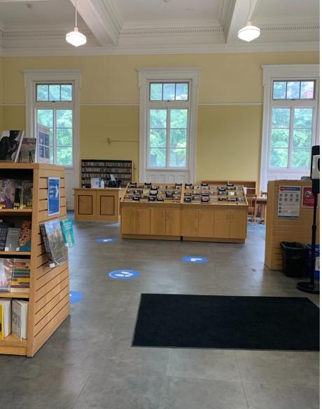 A colour photograph of a large room with three windows, two hanging lights, a black mat and book shelves.