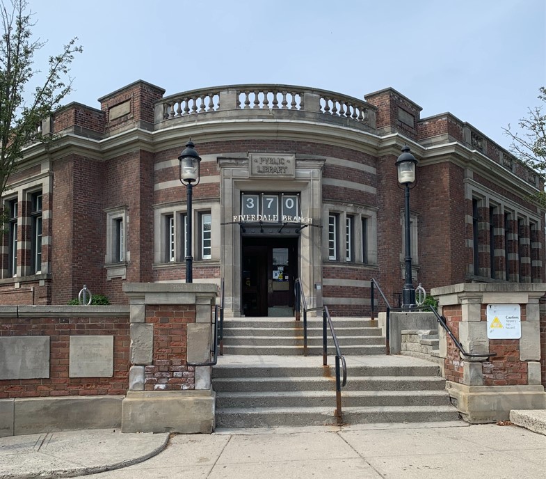 A colour photograph of a brown-brick building with a curved entrance. Two short flights of stairs lead to the building entrance.