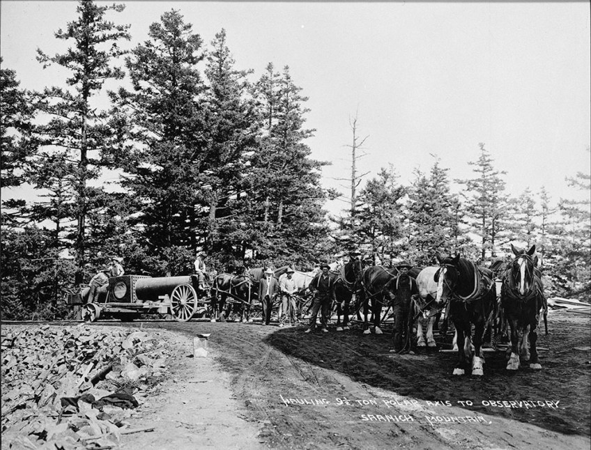 Black-and-white photograph of a group of men posing with a team of horses attached to a wagon carrying part of a telescope.