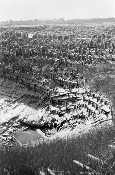 The wooden structure of an old dyke at the edge of a field.
