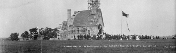 The Acadian Memorial Church under construction, with people gathered in front for a dedication ceremony.