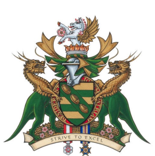 A colour image of a coat of arms. The shield in the centre has three footballs lined up diagonally from the upper left to lower right. There are two dragons, one standing on each side of the shield. The motto reads, “Strive to Excel.”