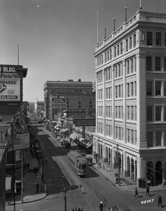 A black-and white-photograph of downtown Calgary, looking down at an intersection, with streetcars, cars and people visible on the streets and sidewalks.