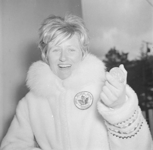 A young woman wearing a winter coat holding a medal in her left hand.