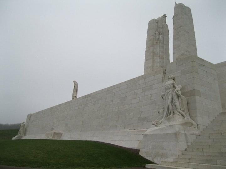 A white stone structure with carved human figures against a foggy sky.