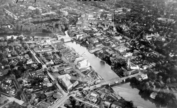 A city with houses and buildings on either side of a river, with a bridge connecting the two sides.