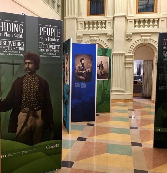 Colour photograph of an exhibition space showing large vertical panels with photographs and texts.